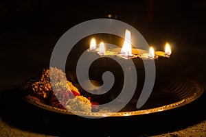 hindu puja essential panch pradeep or five headed oil lamp burning with glowing flame with marigold flowers kept on brass plate.