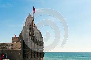 Hindu temple with carved walls a high spire and flag on the coast of blue sea