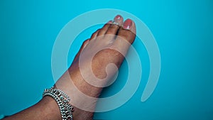 A Hindu woman wearing Silver paajeb Anklets in India. Female foot with red Nail polish isolated on blue background