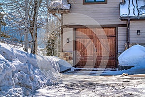 Hinged wooden garage door and snowy driveway viewed at the exterior of home