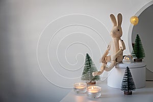 hinged wooden hare, a small artificial green Christmas tree and lighted candles in candlesticks on a white chest of drawers.