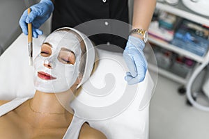 Hingh-angle shot of a woman laying down with her eyes closed while having face mask put by a beautician. Beauty concept.