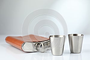 Hip flask and cups on white table. Space for text