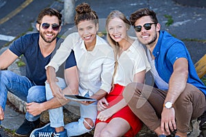 Hip friends looking at tablet and sitting on sidewalk