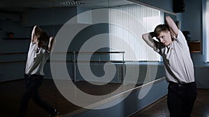 Hip hop dancer performing his dance standing near the mirror in the dance studio. Smooth honed motion of young guy.