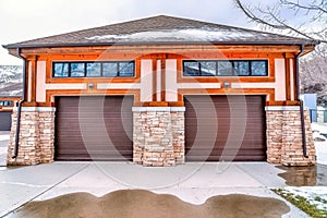 Hip roof garage exterior with two brown doors and wet snowy driveway in winter.