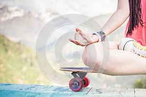 Hippie fashion girl doing yoga, relaxing on skateboard at mountain