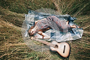 Hippie girl with guitar lying on the mowed grass
