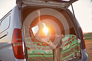 a hippie girl lies upside down in a minivan in an open field