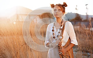 Hippie girl in ornaments boho chic stands in a field at sunset