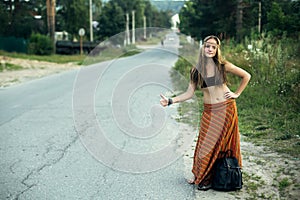 A hippie girl voting near the country road. Hitchhiking trips.