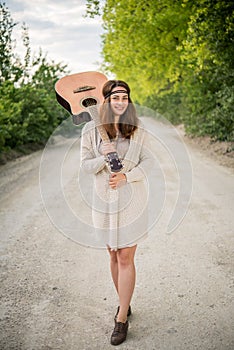 Hippie girl walking on the road with a guitar