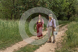 Hippie guy and girl with a retro cassette recorder walk along a country road