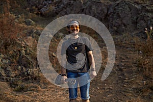 a hippie guy in sunglasses stands in a clearing near the rocks smiling