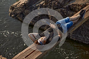 a hippie man with glasses lies on a wooden bridge over the river