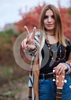 Hippie musician with acoustic guitar, showing piece sign with two fingers. Three-quarter portrait of young woman, wearing colorful