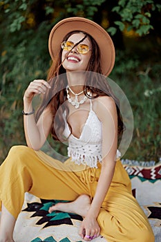 Hippie woman in eco clothing laughs and wiggles as she sits on a plaid outside in the fall with a hat and yellow