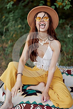 Hippie woman in eco clothing laughs and wiggles as she sits on a plaid outside in the fall with a hat and yellow