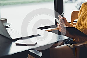 A hipster asian woman working with laptop and writing information into notebook