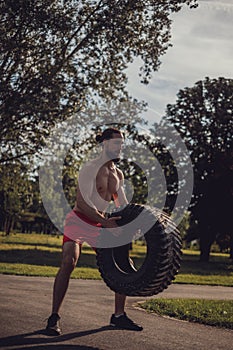 Hipster athlete trying to lift tire in the park