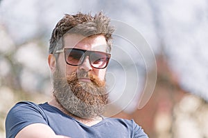 Hipster with beard and mustache on strict face, nature background, defocused. Bearded guy wears stylish sunglasses. Man