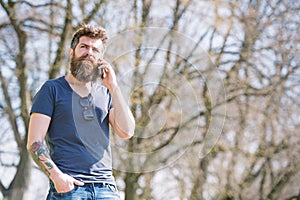 Hipster with beard speak on mobile phone outdoor. Man with beard and mustache on strict face talking, nature background