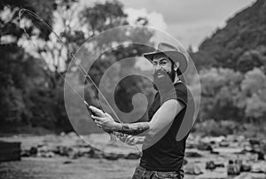 Hipster bearded man catching trout fish. Man with fishing rod, fisherman men in river water outdoor. Summer fishing