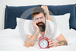 Hipster bearded man lay in bed with alarm clock. Time to wake up. Why you should wake up early every morning. Health