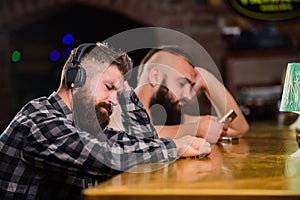 Hipster bearded man spend leisure at bar counter. Order drinks at bar counter. Men with headphones and smartphone