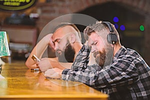 Hipster bearded man spend leisure at bar counter. Order drinks at bar counter. Men with headphones and smartphone