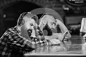 Hipster bearded man spend leisure at bar counter. Order drinks at bar counter. Men with headphones and smartphone