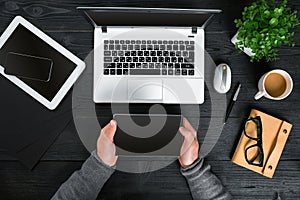 Hipster black wooden desktop top view, male hands typing on a laptop