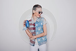 Hipster blonde girl in american patriotic outfit and sunglasses holding soda can isolated on grey