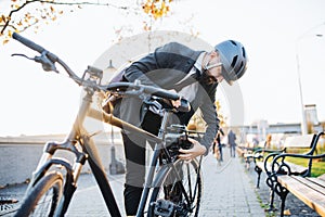 Hipster businessman commuter setting up electric bicycle in city.