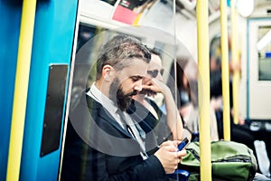 Hipster businessman with smartphone inside the subway in the city, travelling to work.