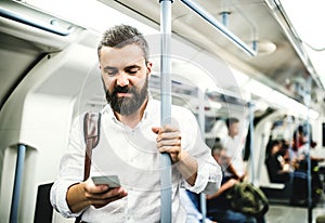 Hipster businessman with smartphone inside the subway in the city, travelling to work.