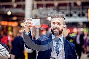 Hipster businessman with smartphone taking selfie, crowded train