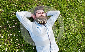 Hipster on calm face lays on grass, top view. Appeasement concept. Guy looks nicely with daisy or chamomile flowers in