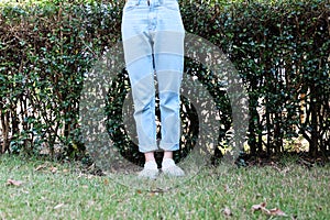 Hipster Casual White Sneakers. Female Standing Wearing White Shoes and Blue Jeans Pants on Green Grass Nature Background