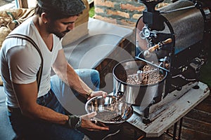 Hipster catching roasted coffee from the roaster with a dish