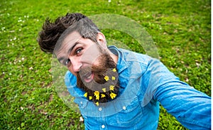 Hipster on cheerful face sits on grass, defocused. Man with beard enjoys spring, green meadow background. Natural beauty