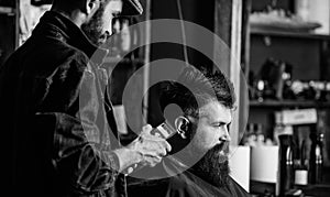 Hipster client getting haircut. Barber with hair clipper works on haircut of bearded guy, retro barbershop background