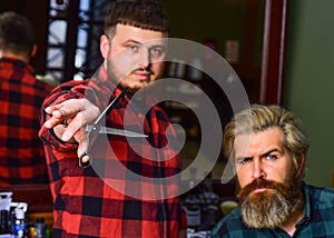 Hipster client getting haircut. Barber with scissors and client. Barber works on hairstyle for bearded man barbershop