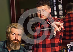 Hipster client getting haircut. Barber with scissors and client. Barber works on hairstyle for bearded man barbershop