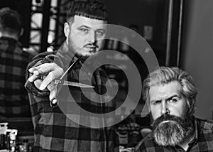 Hipster client getting haircut. Barber with scissors and client. Barber works on hairstyle for bearded man barbershop