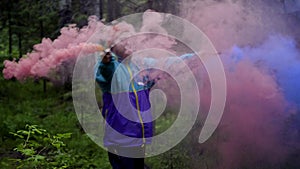 Hipster with colored smoke bombs in forest. Stock footage. Young man dispels colored smoke bombs in green forest for