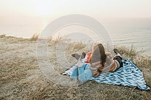 Hipster couple chilling and hugging on blanket on rocky coast wi