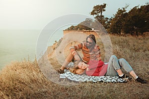 Hipster couple chilling and hugging on blanket on rocky coast wi