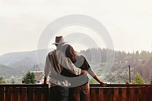 Hipster couple hugging on porch of wooden house looking at mount