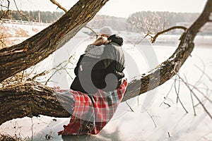 Hipster couple sitting on tree over frozen lake